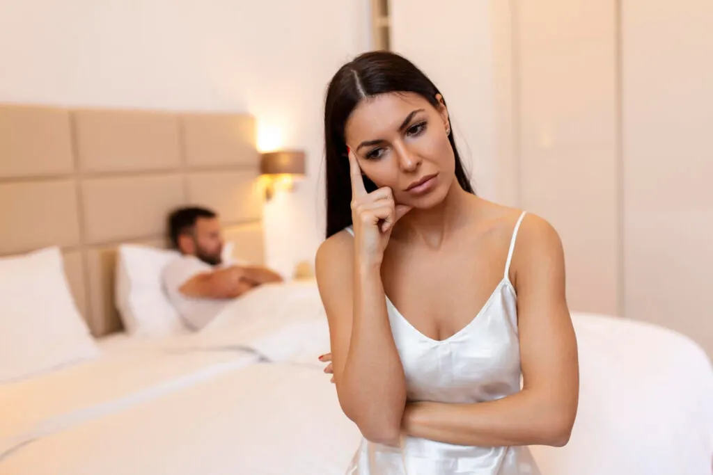 Mujer preocupada sentada en la cama mientras su pareja duerme