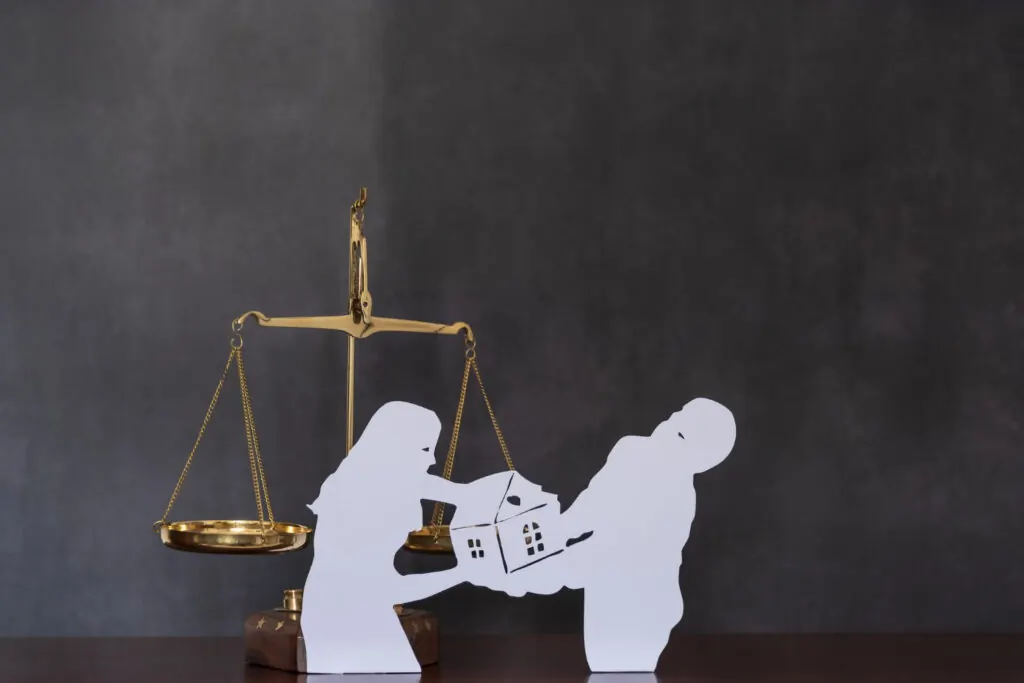 Silueta de una pareja que se disputa una casa frente a una balanza de la justicia